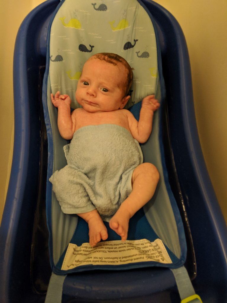 newborn lying in blue baby bath tub with sling