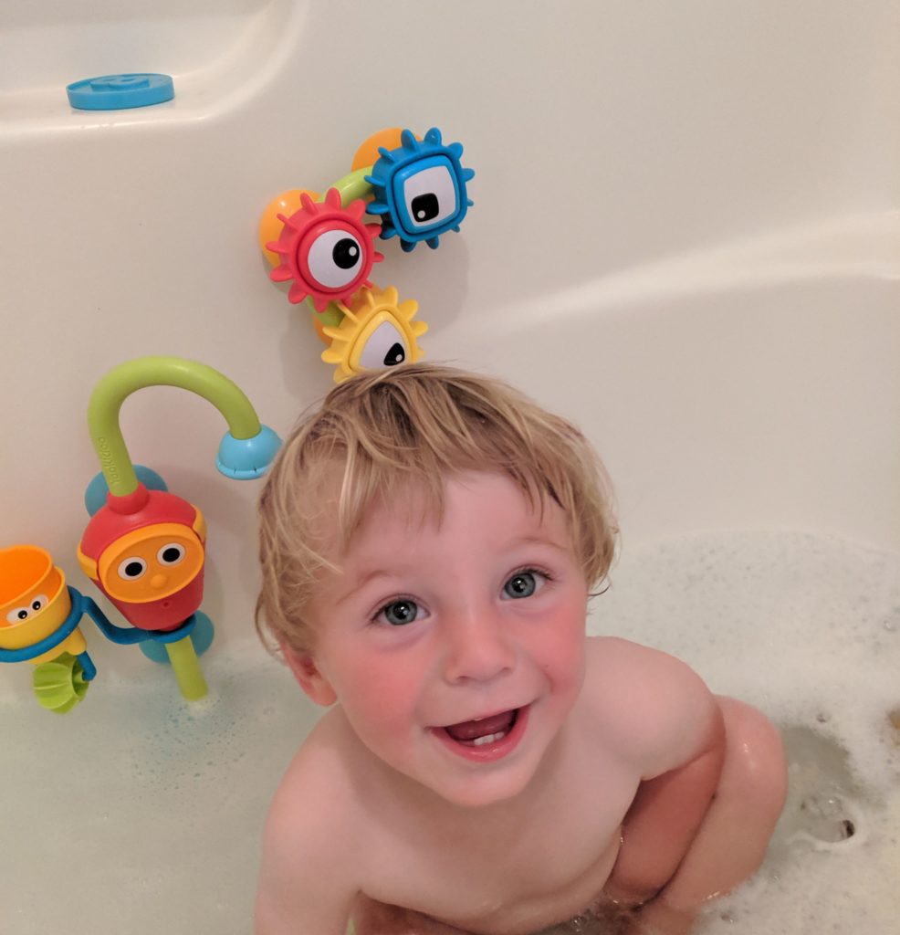 laughing toddler in bathtub with Yookidoo Flow 'n Fill baby bath toy
